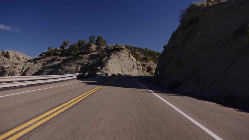 A smooth point-of-view drive along a scenic highway carved through rocky canyons on a bright, sunny day