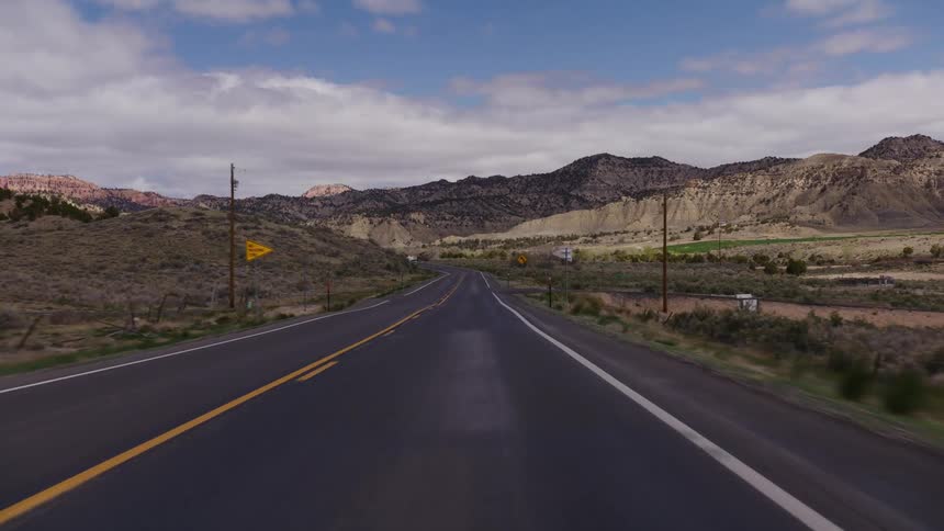 A driver's point-of-view shot traveling along a winding two-lane highway through a vast, rural mountain valley