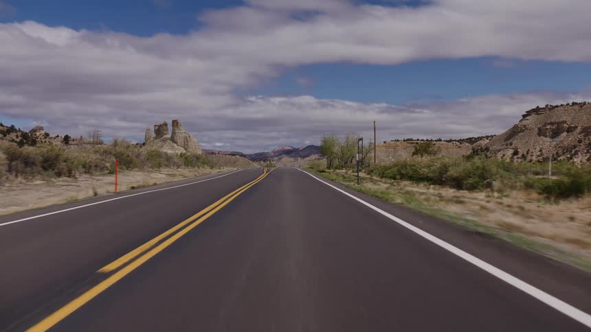 A scenic point-of-view drive down an open highway through a vast desert landscape under a partly cloudy sky