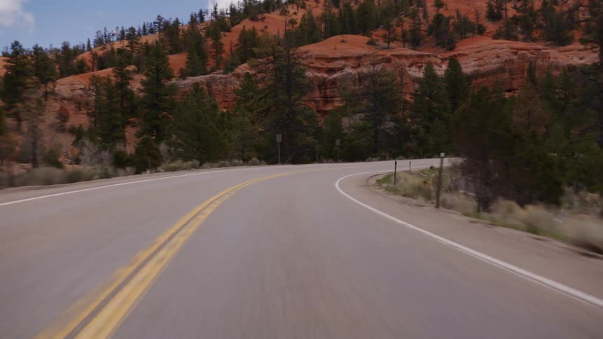 A point-of-view drive along a scenic highway winding through red rock mountains and pine forests