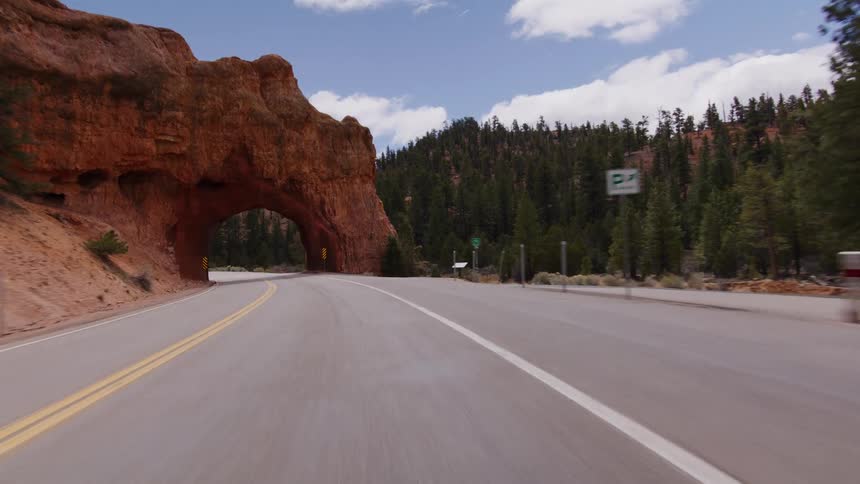 A point-of-view drive along a winding road leads through a tunnel carved into the Red Canyon Arch in Utah