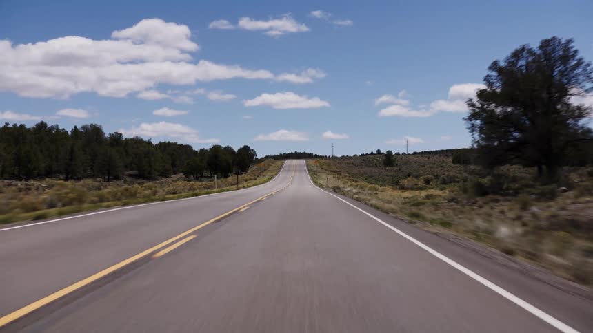 Point-of-view shot driving along a long, empty highway through a high desert landscape on a sunny day