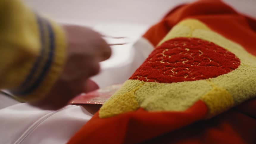 An artist carefully applies hot glue to a piece of red and yellow tufted fabric in a workshop setting