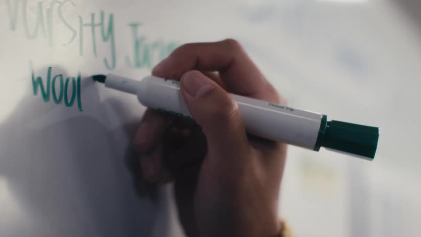 A close-up slow motion shot of a hand writing on a white board with a green marker