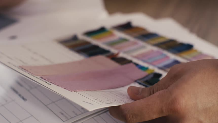 A designer carefully examines colorful fabric swatches from a sample book, selecting the perfect material for a new project