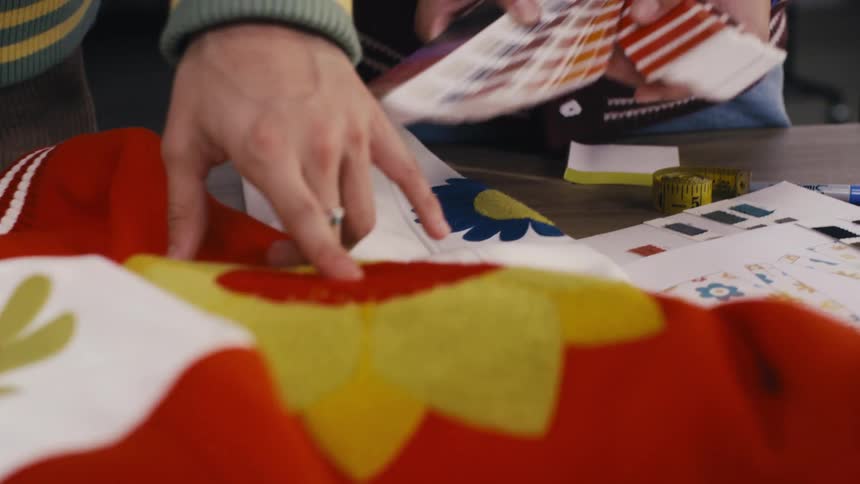 Two fashion designers collaborate on a colorful floral garment, using color swatches to perfect their design in a studio