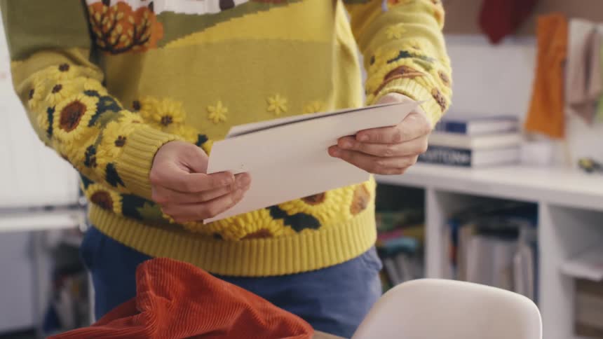 A person wearing a bright yellow sunflower sweater opens and reviews sheets of white paper in their studio