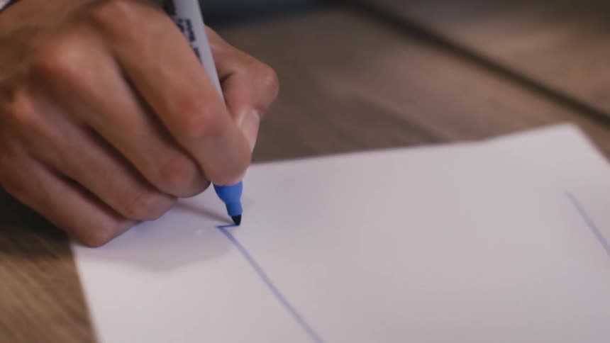 A person's hands meticulously draw a series of blue lines on a blank sheet of white paper with a marker