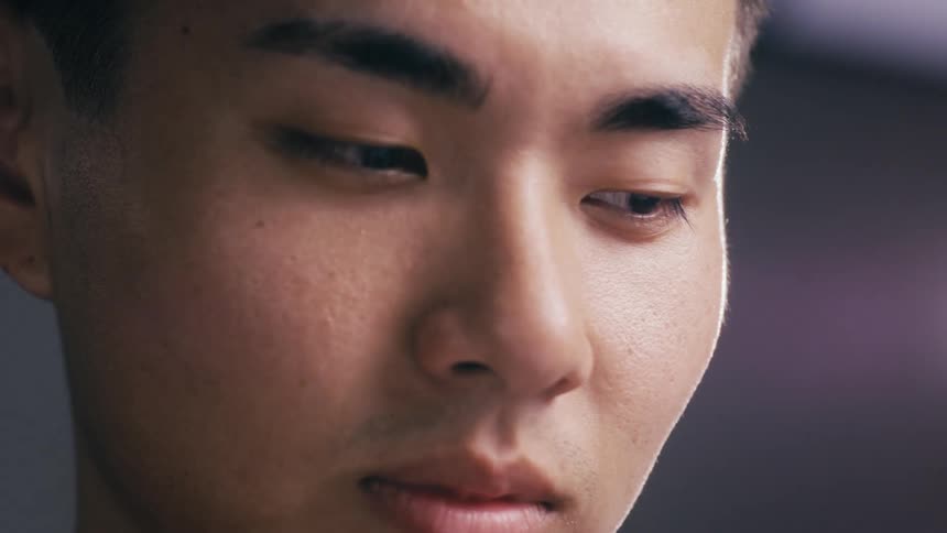 Extreme close-up on the face of a young Asian man looking down in deep concentration