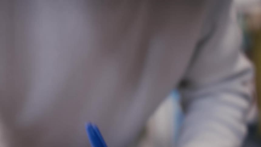 A young man with a focused expression carefully writes a message on a white envelope with a blue marker
