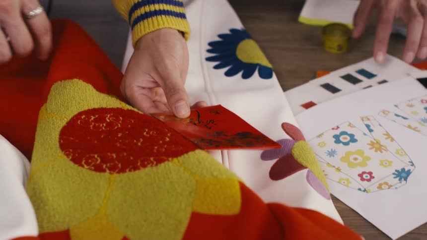 Fashion designers collaborate on a colorful floral jacket, comparing fabric swatches and sketches in their studio