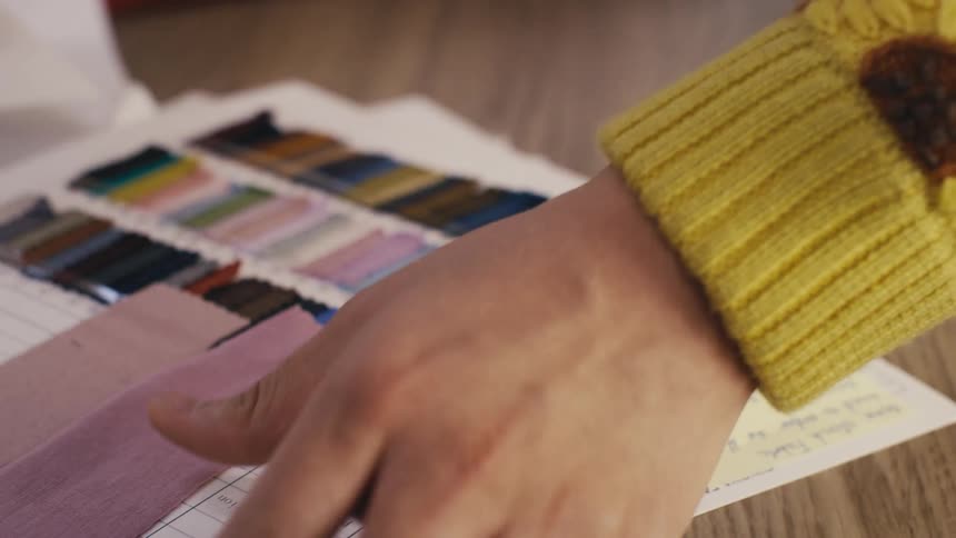 Slow-motion close-up of a designer's hands flipping through a book of colorful fabric swatches