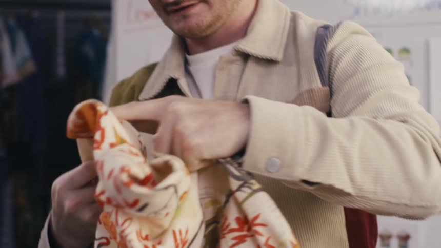 A young male fashion designer meticulously inspects the details and fabric of a colorful patterned shirt in his studio