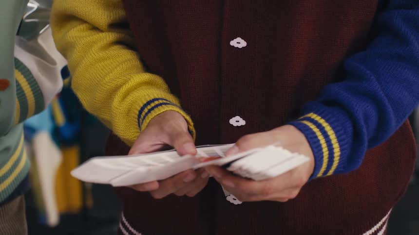 A designer wearing a multi-colored varsity jacket fans through color swatches in a creative studio