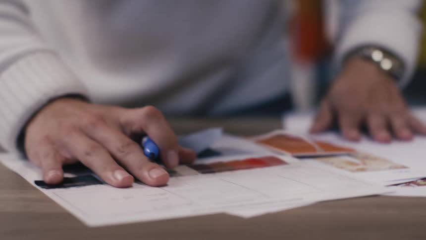 A designer wearing a gold watch reviews mood board images and sketches a new concept with a blue marker