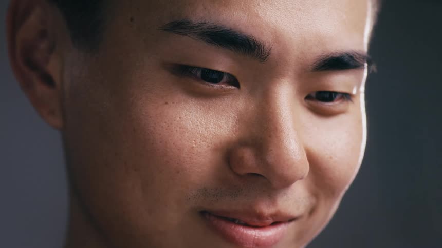 A very close-up shot of a young East Asian man's face as he looks down with a content expression