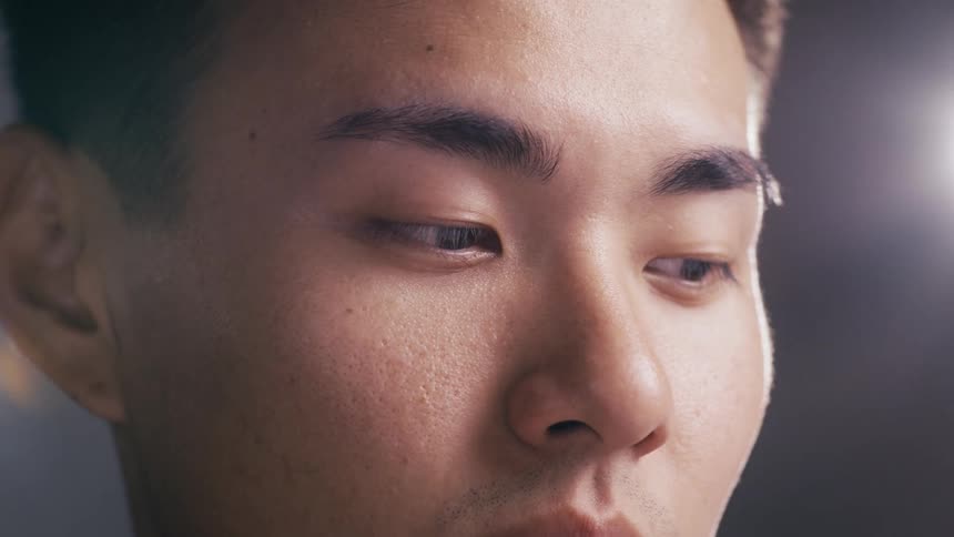 A detailed macro shot captures the contemplative gaze of a young Asian man