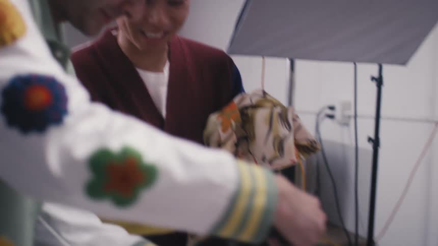 A smiling photographer and fashion designer collaborate during a product photoshoot for a colorful retro clothing line in a studio