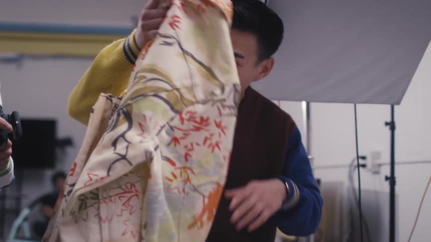A photographer and an assistant meticulously arrange a vintage floral shirt for a product photoshoot in a studio