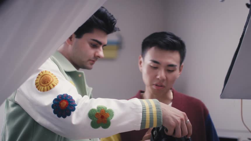 A photographer and a stylist collaborate on a product photoshoot, arranging and capturing images of a colorful clothing collection in a studio