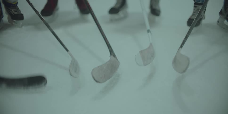 A close-up view shows hockey players tapping their sticks on the ice in unison as a sign of respect