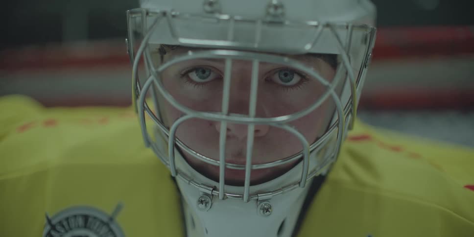 An intense ice hockey goalie stares directly into the camera from behind his protective face mask