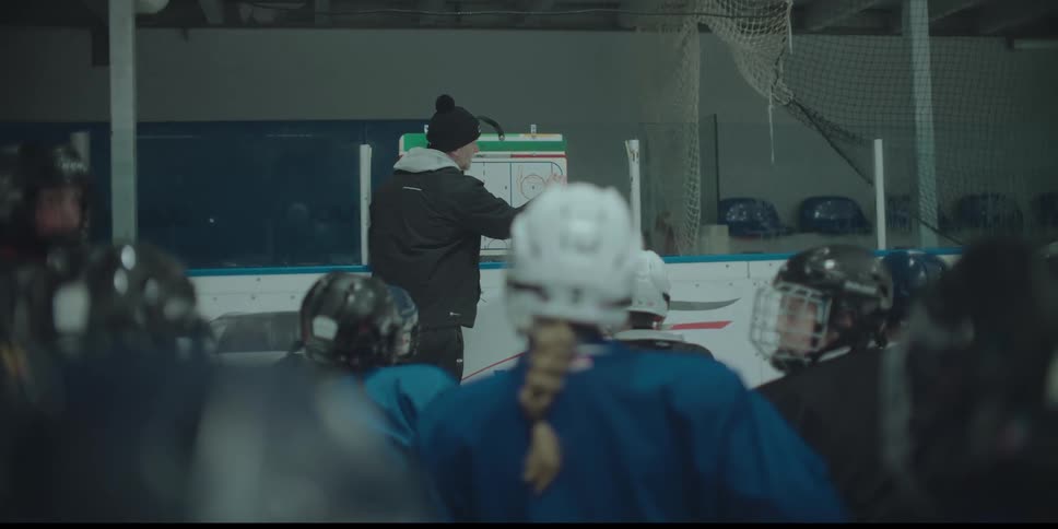 An ice hockey coach draws up a play on a whiteboard for his female team during a practice at the rink