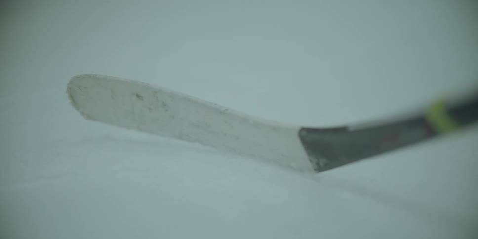 A tight, shallow focus shot of a white hockey stick blade resting on the ice of a rink