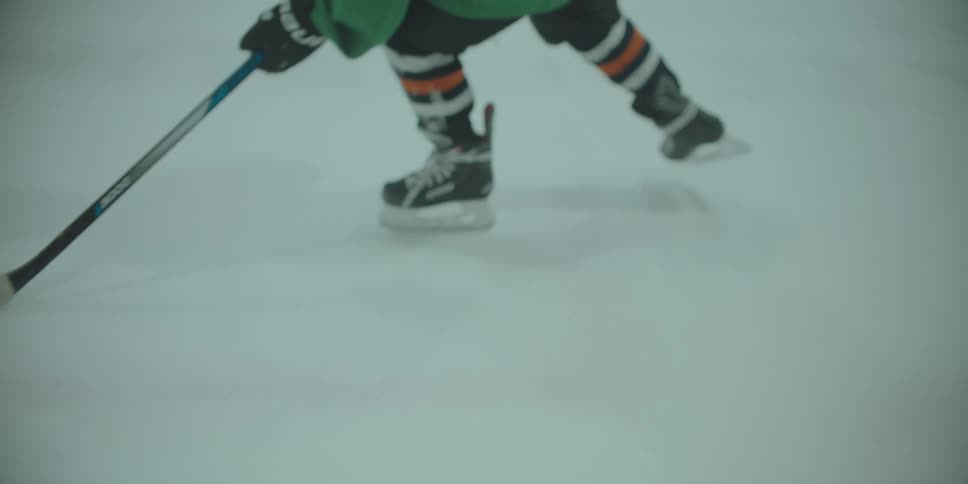 Close-up slow-motion shot of a young hockey player's skates and stick as they practice stickhandling a puck around a cone on the ice