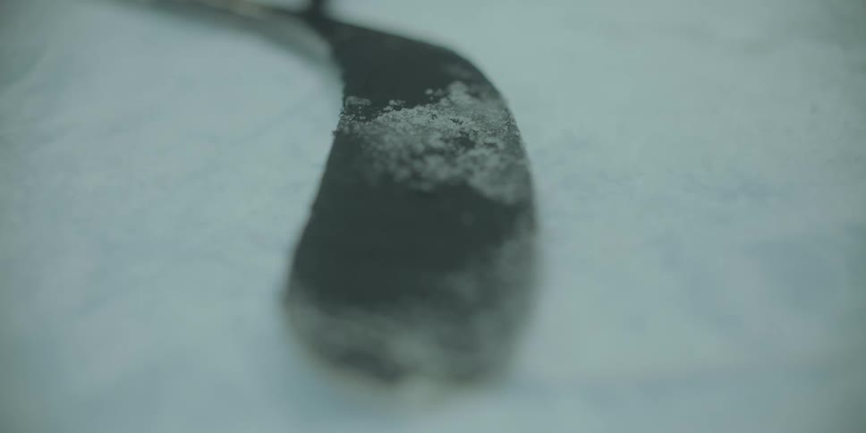 A close-up of a hockey stick blade covered in snow resting on the ice