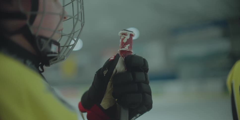Close up of a young hockey player's gloved hand holding a hockey stick handle on the ice rink