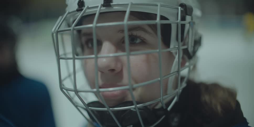 A close-up portrait of a determined young female ice hockey player in a helmet