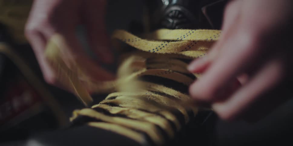 A detailed close-up shot shows a person's hands methodically tying the yellow laces of a black hockey skate