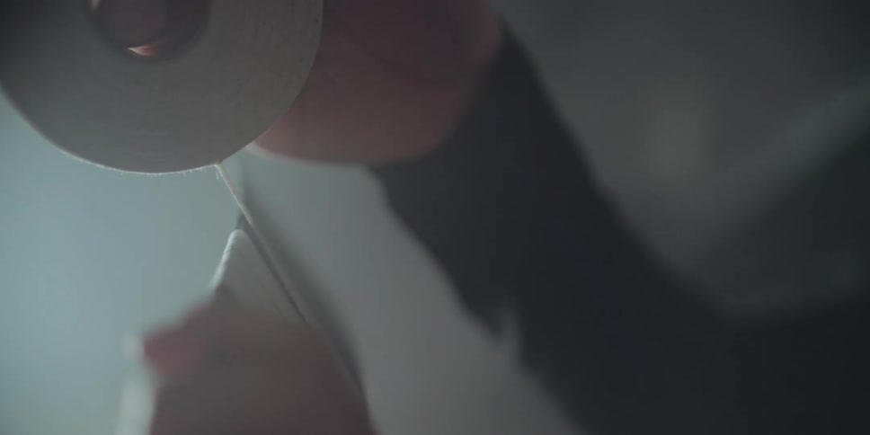 A slow-motion, low-angle close-up of a person carefully wrapping the blade of a hockey stick with white tape