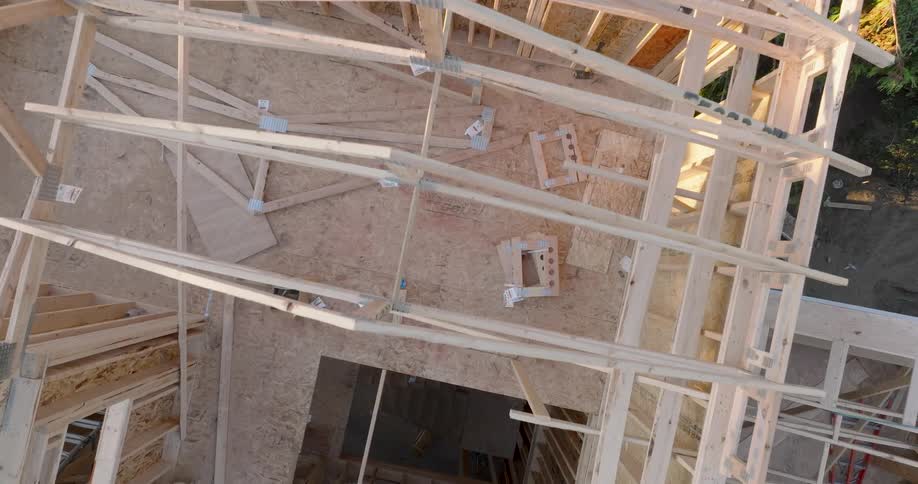 Birds eye view above new roof rafters and wooden framework of a multi-story house under construction