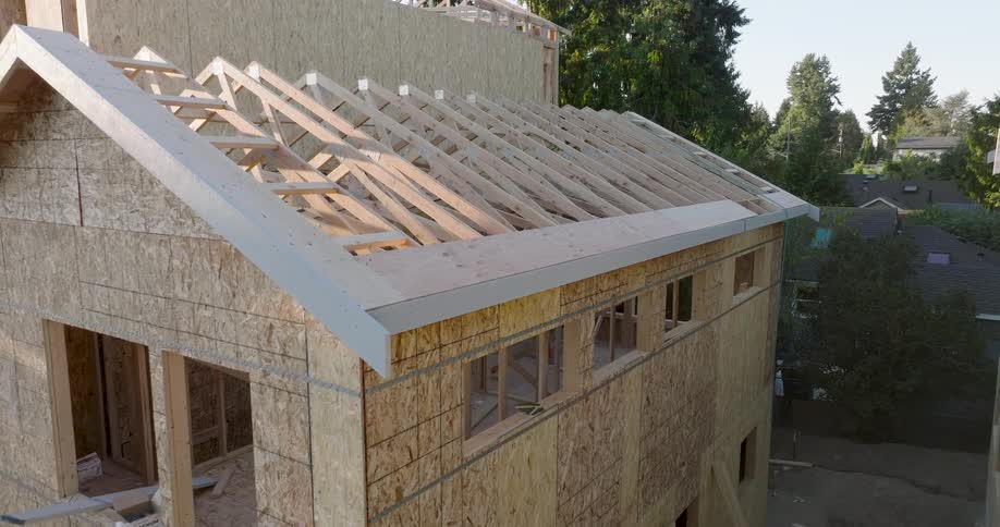 Slow pull back from sun kissed roof trusses to reveal a new home being framed at a residential construction site