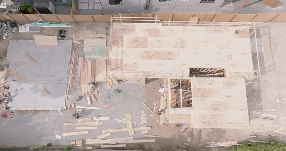 Slow descent towards construction workers framing the walls and sub-floor of a new residential building