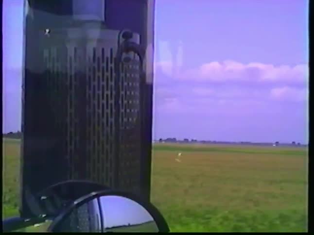 A vintage point-of-view shot from a truck driving past vast rural cornfields and onto a sunny highway