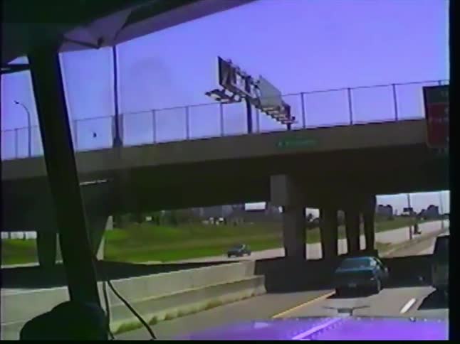 Vintage point-of-view footage from a semi-truck driving on a highway towards the Minneapolis city skyline on a sunny day