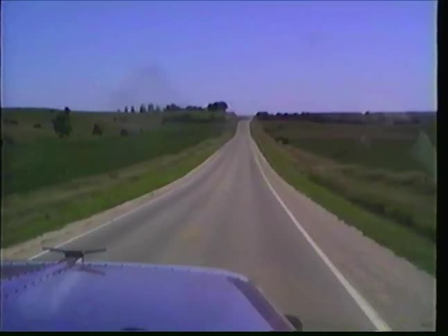 A vintage point-of-view shot from a car driving on a rural highway, passing an Amish horse and buggy on a sunny day