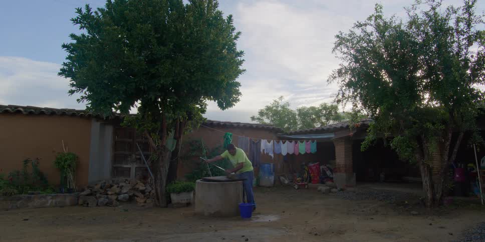 A man hand washes laundry at a well in a rural courtyard with hanging clothes