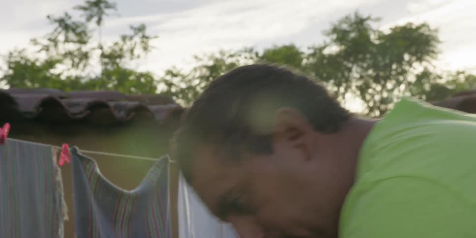 A close-up profile of a man in conversation outdoors with a clothesline in the background
