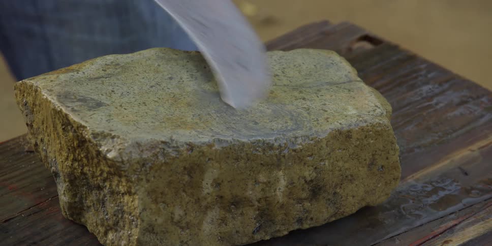 A close-up shot of a person sharpening a curved metal blade on a large whetstone