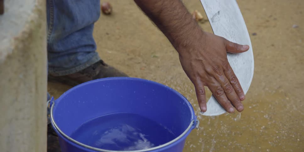 Close up in slow motion of a man's hands washing a large curved blade with water from a blue bucket