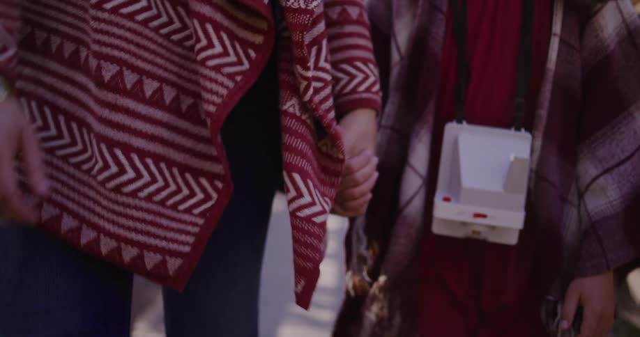 A mother and daughter in cozy sweaters hold hands while walking across a sunny bridge in slow motion