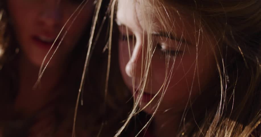 A soft-focus, slow-motion close-up of a young girl with her mother looking on in the background