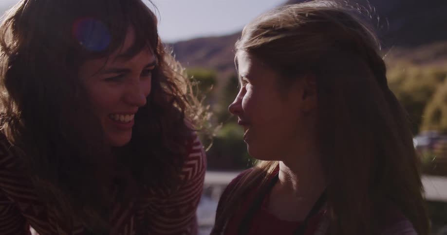 A smiling mother and her young daughter share an intimate conversation while enjoying a sunny day outdoors in slow motion