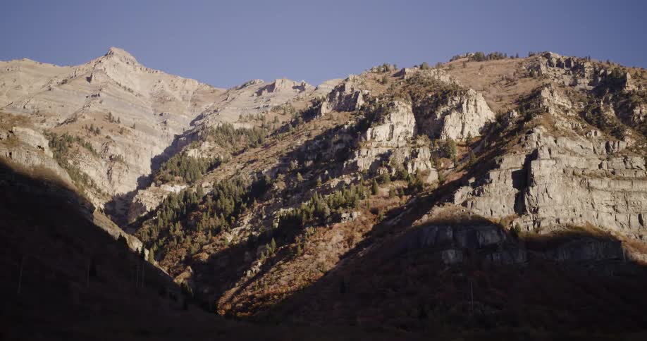 A slow, scenic drive through a shadowy valley reveals the vast, sunlit cliffs of a majestic mountain range