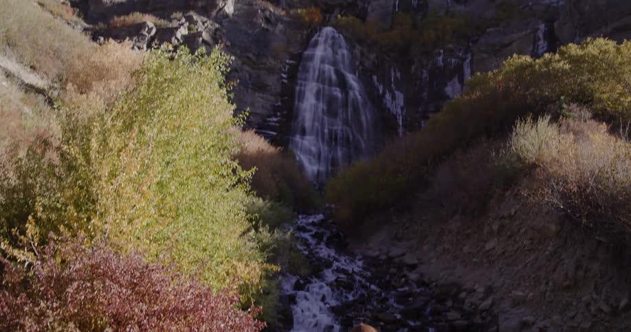 A mother and daughter explore a mountain stream as the camera tilts up to reveal a beautiful waterfall during autumn