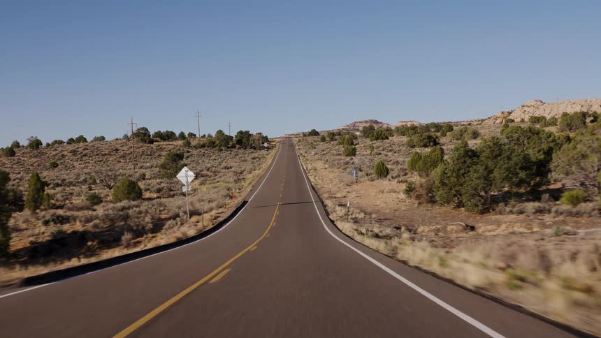 Driving POV down a long, straight desert highway that disappears over a distant hill on a clear day